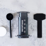 All of what is included with the AeroPress Original Coffee Maker, including a measuring cup, stirring spoon, and AeroPress filters | Equator Coffees