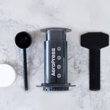 All of what is included with the AeroPress Original Coffee Maker, including a measuring cup, stirring spoon, and AeroPress filters | Equator Coffees
