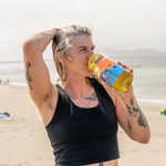 A woman on a beach drinking from a yellow and blue Golden Hour Nalgene bottle | Equator Coffees