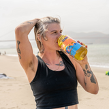 A woman on a beach drinking from a yellow and blue Golden Hour Nalgene bottle | Equator Coffees