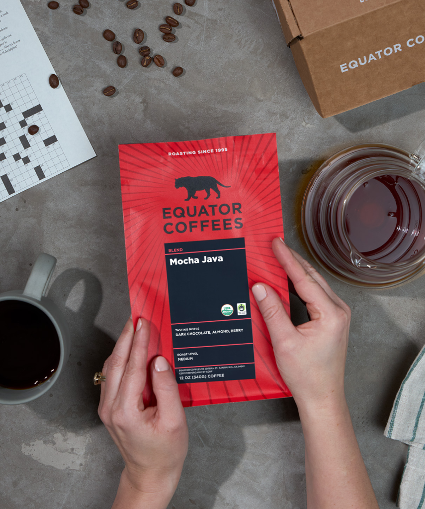 Person holding an Equator Coffees Mocha Java package on a table | Equator Coffees