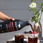 Smooth Black Organic Cold Brew Coffee | Pouring a couple of glasses of refreshing cold brew coffee over ice | Front of 42 fl oz bottle | Equator Coffees