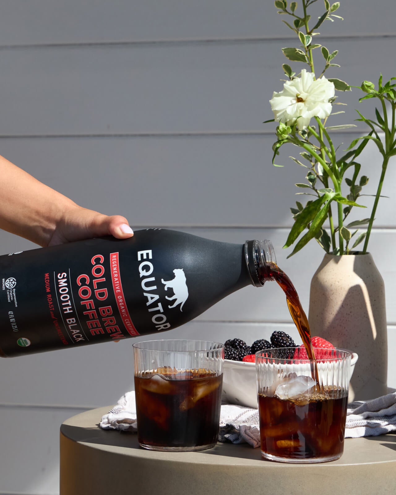 Smooth Black Organic Cold Brew Coffee | Pouring a couple of glasses of refreshing cold brew coffee over ice | Front of 42 fl oz bottle | Equator Coffees